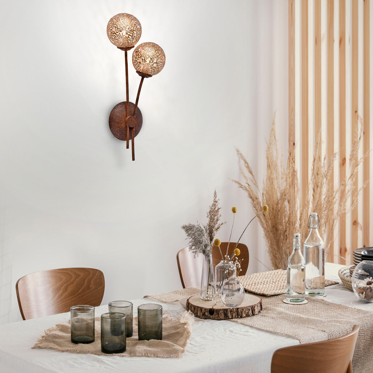 Mise en ambiance : applique murale allumée au-dessus d'une table dressée avec fleurs séchées.