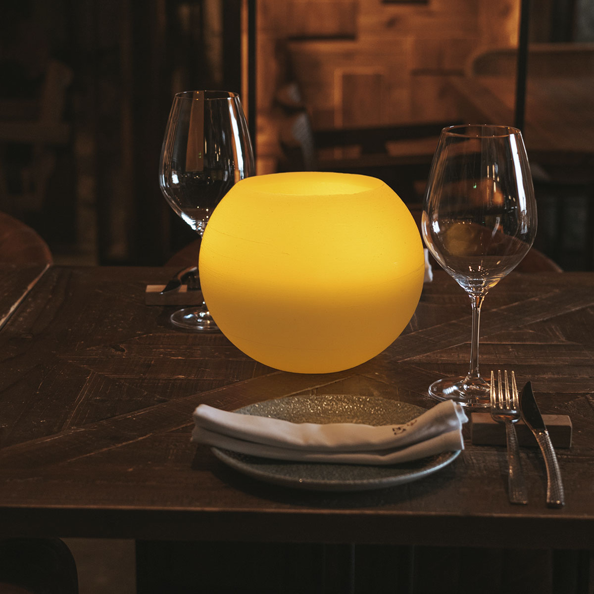 Boule lumineuse jaune sur table en bois avec verres à vin