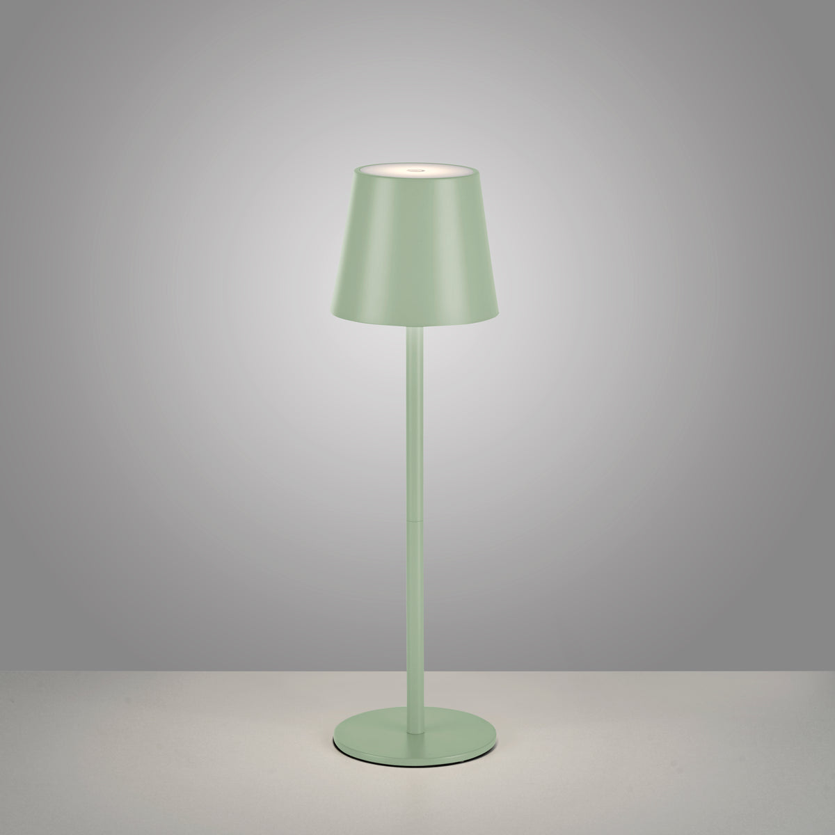 Photo studio sur fond gris clair, lampe allumée, abat-jour conique et tige fine.