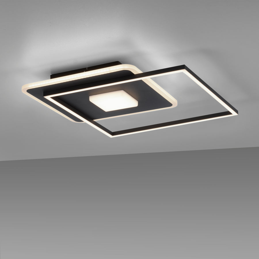 Luminaire allumé vu en plongée, cadres carrés noirs et blancs superposés au plafond.