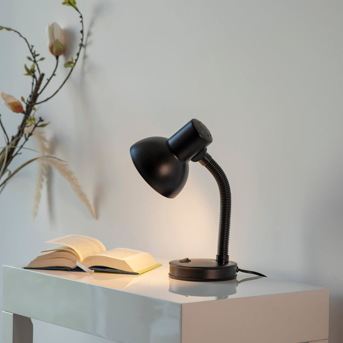 Mise en ambiance sur une console blanche, lampe allumée près d'un livre ouvert.