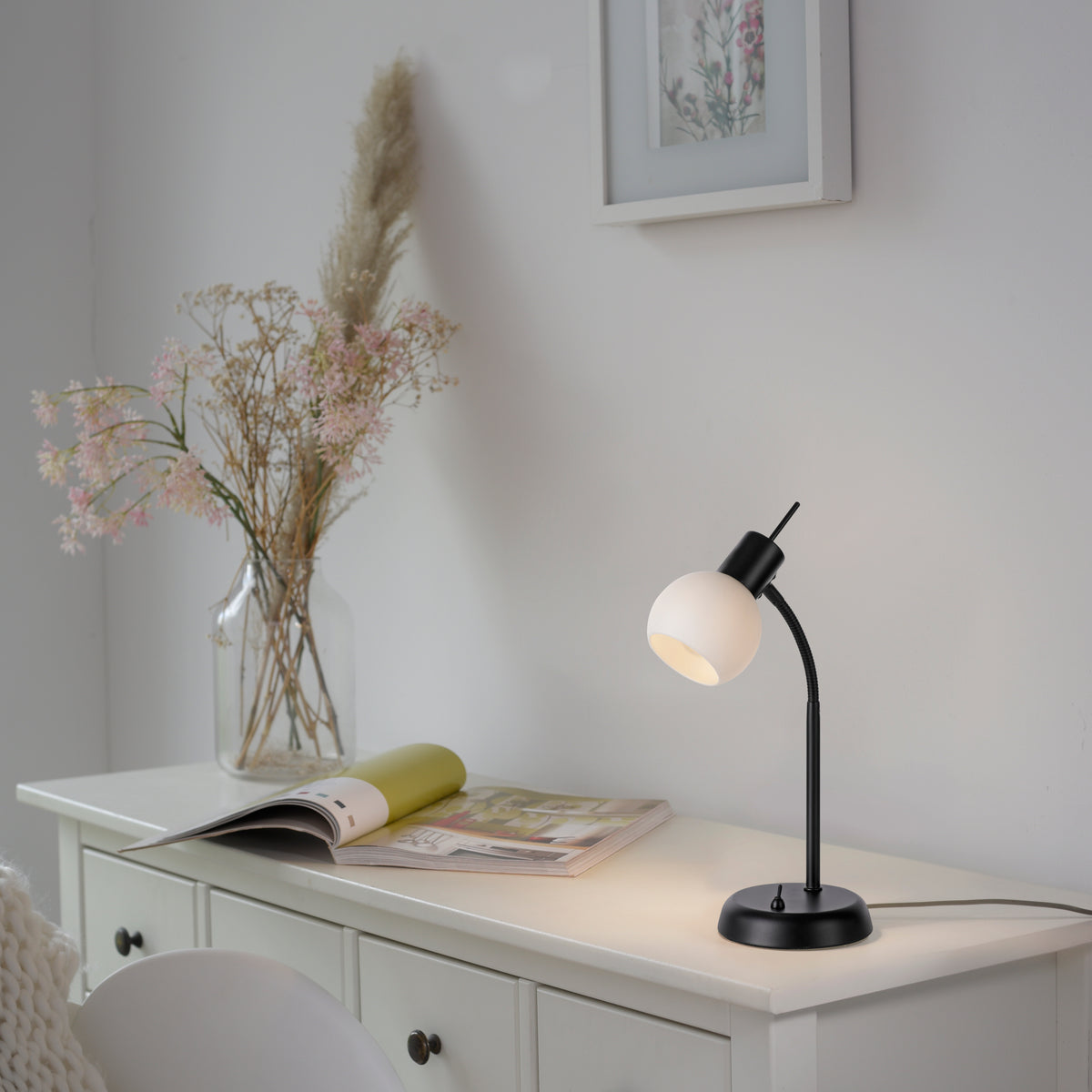 Mise en ambiance : lampe posée sur un meuble blanc, près d’un vase et d’un magazine.