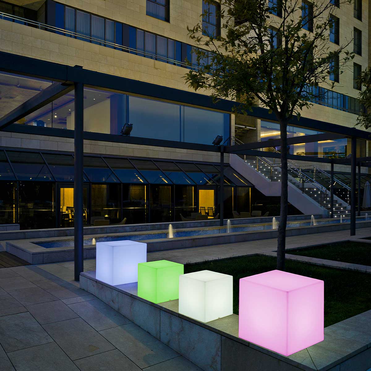 Quatre cubes lumineux colorés alignés devant un bâtiment moderne, mise en ambiance