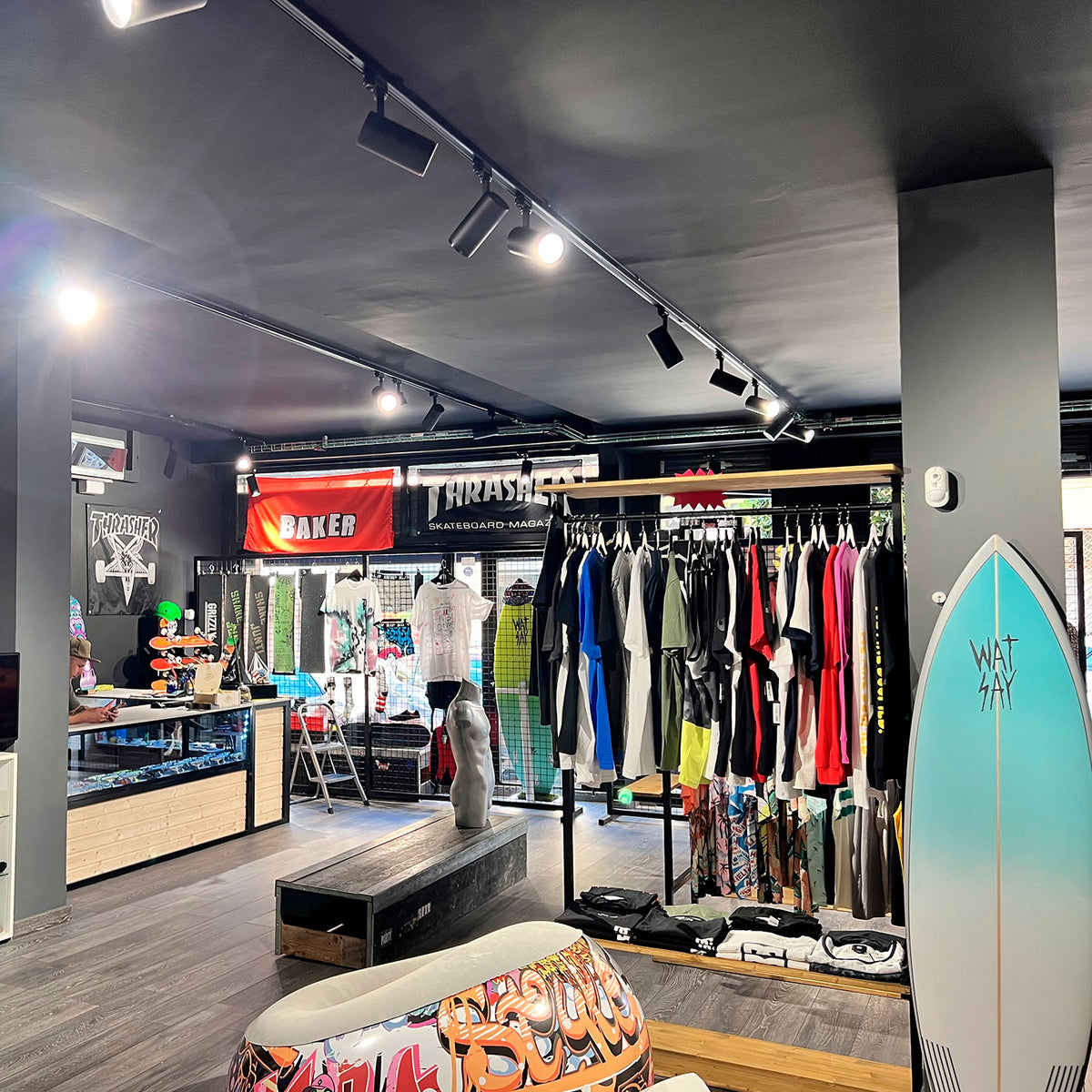 Mise en ambiance dans un magasin de skate, rails noirs au plafond et vêtements colorés.