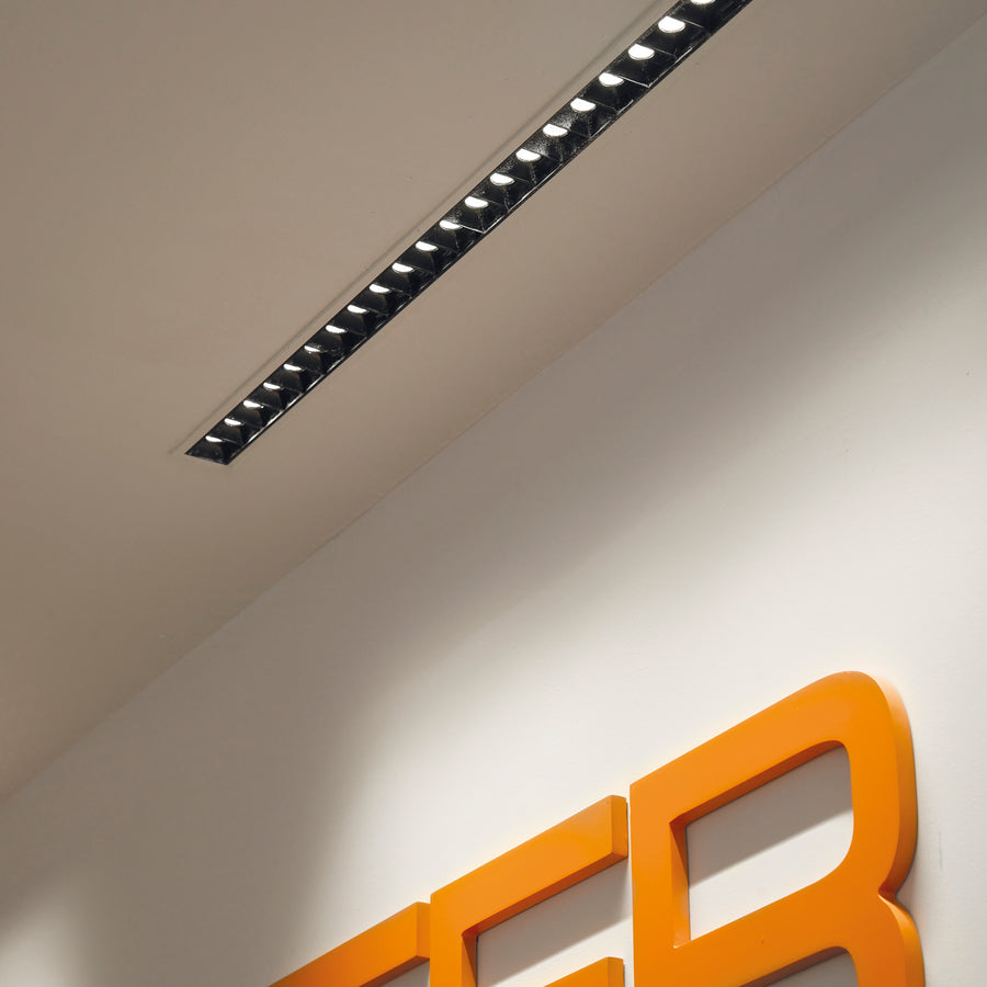 Mise en situation au plafond, éclairant un logo orange mural dans un espace blanc.