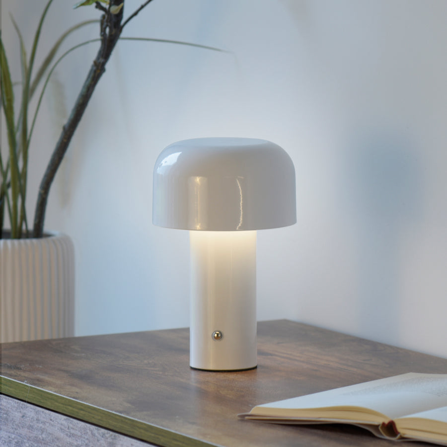 Lampe allumée posée sur table en bois, près d'une plante et d'un livre ouvert.