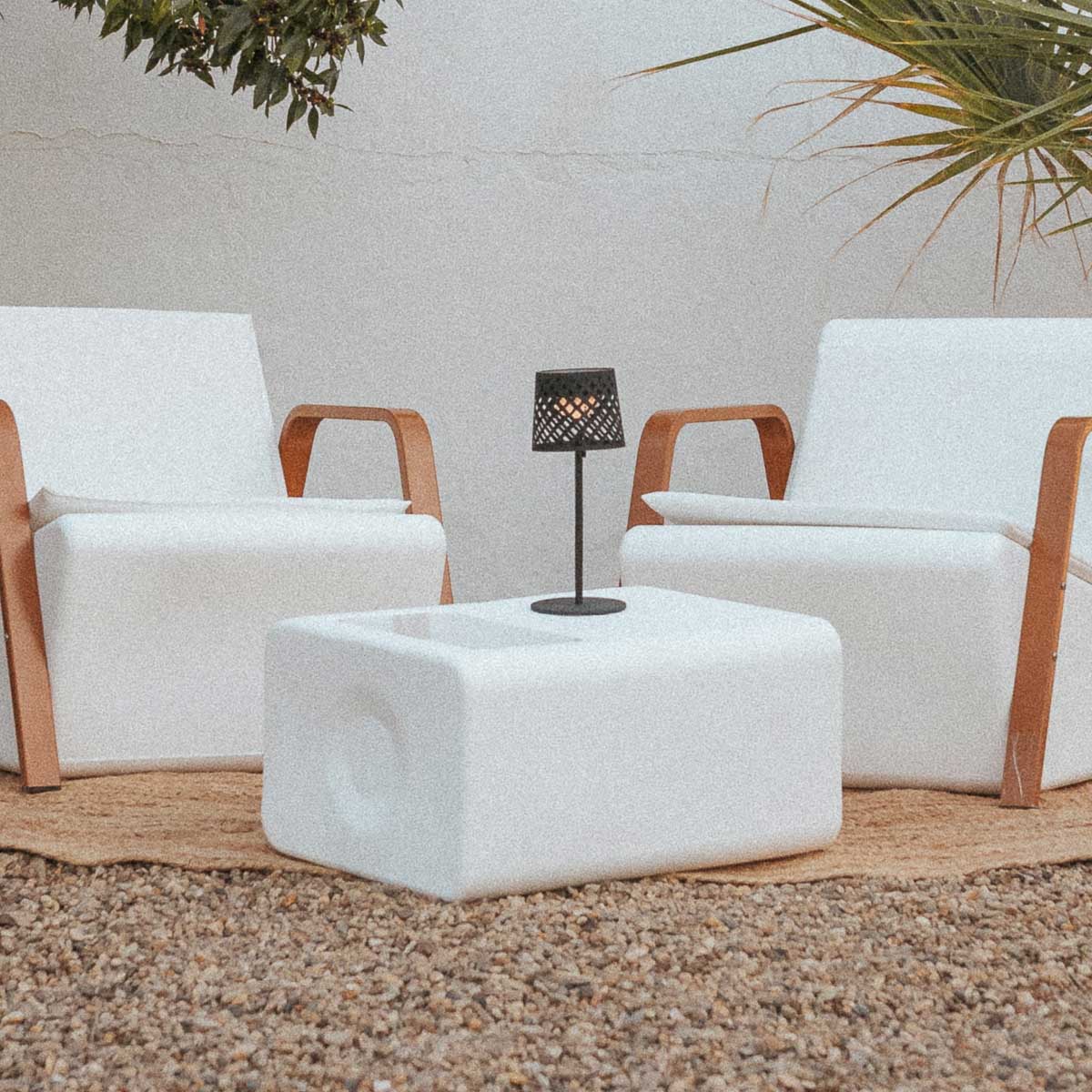 Lampe à poser noire sur table basse blanche, extérieur avec chaises en bois.