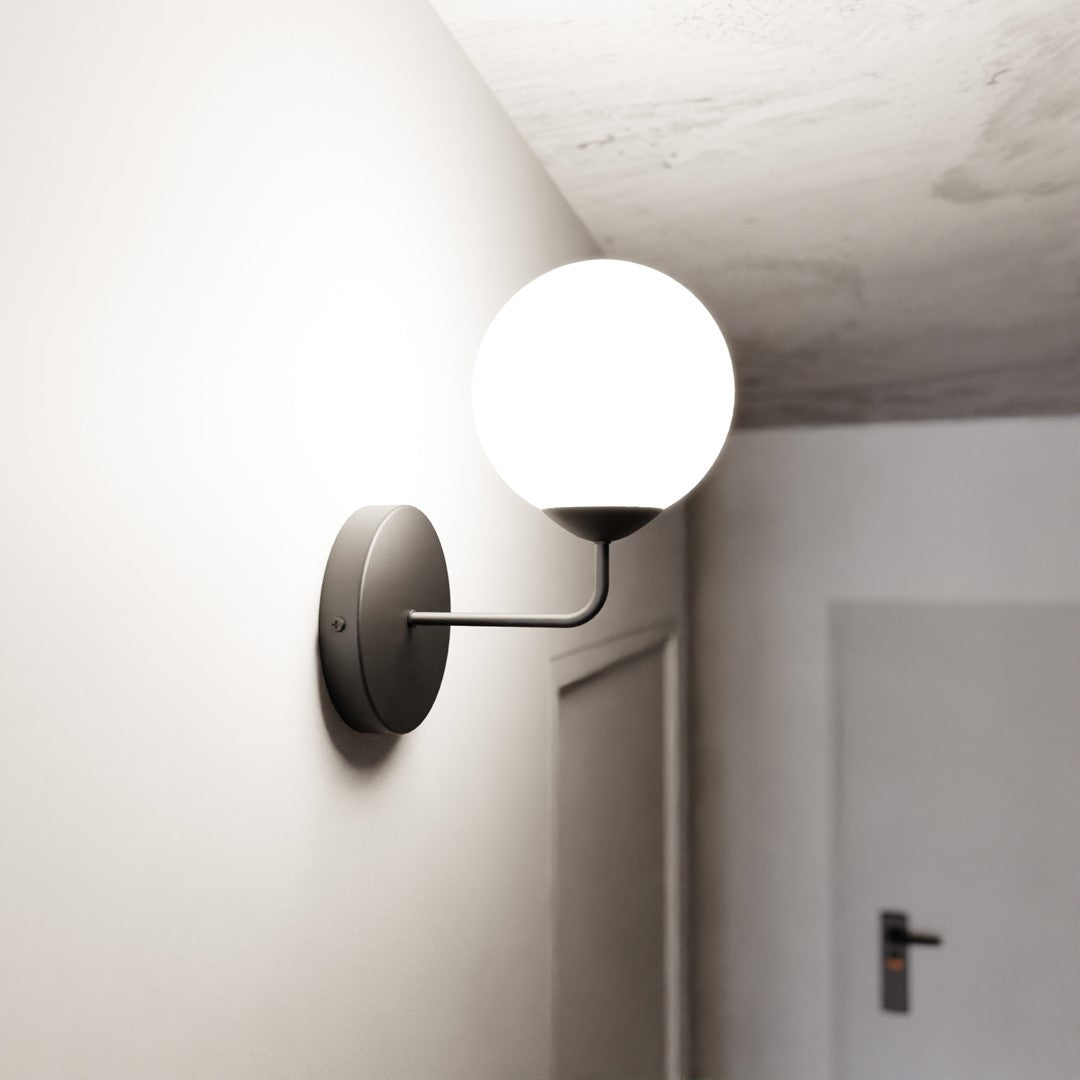 Mise en ambiance dans un couloir : applique allumée sur mur blanc près d'une porte.