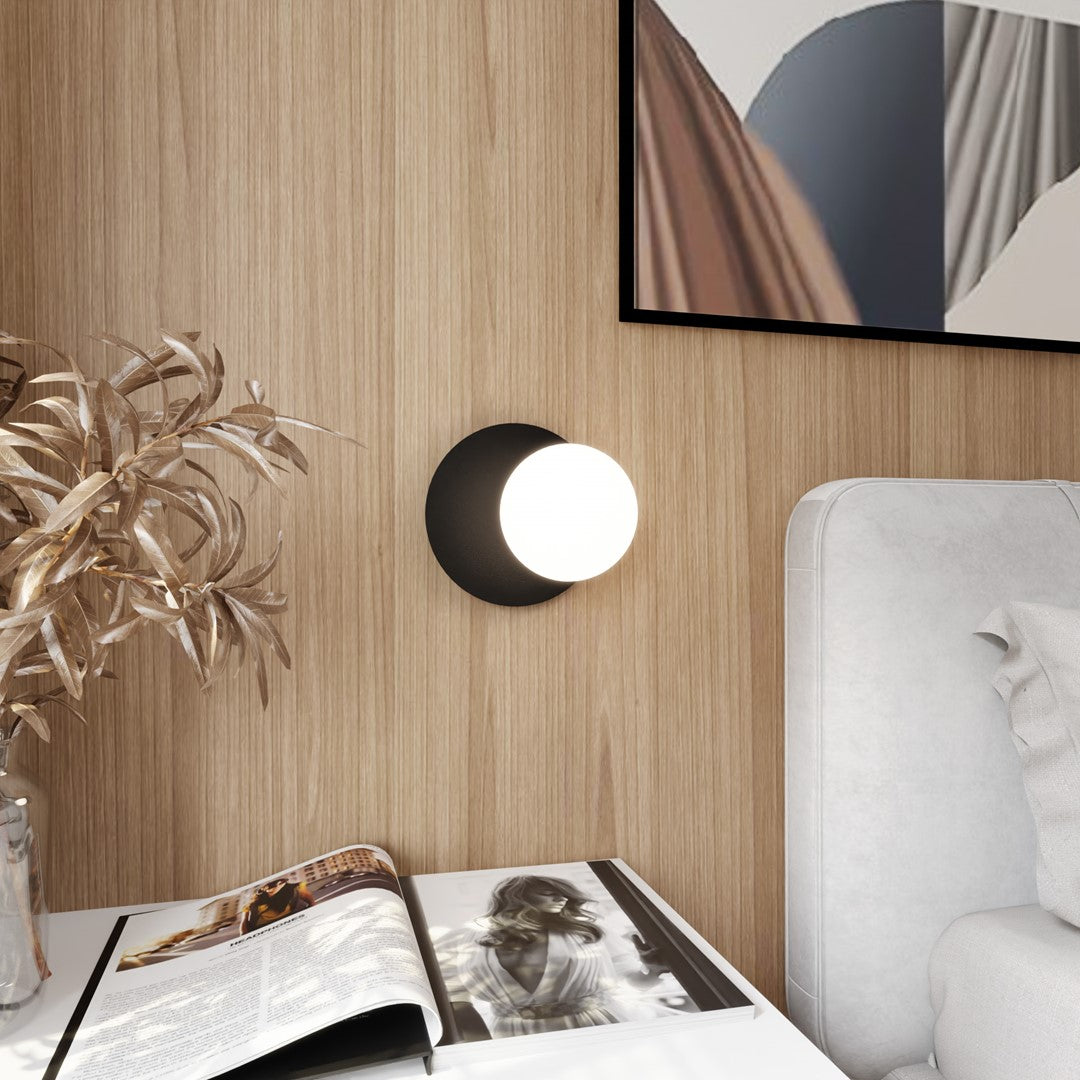 Mise en ambiance : applique murale noire allumée sur une tête de lit en bois clair.