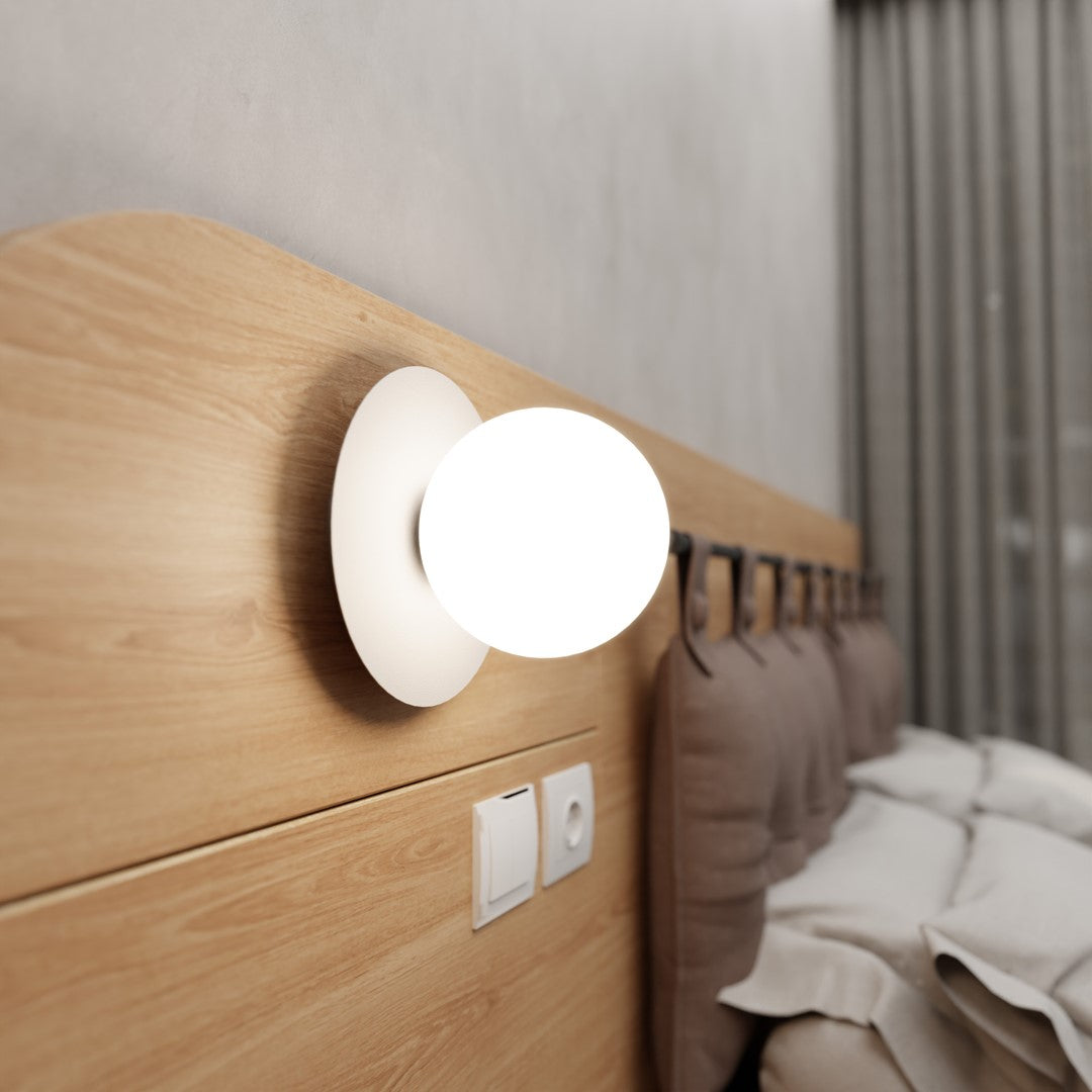Mise en ambiance près d'une tête de lit en bois, applique allumée côté droit.