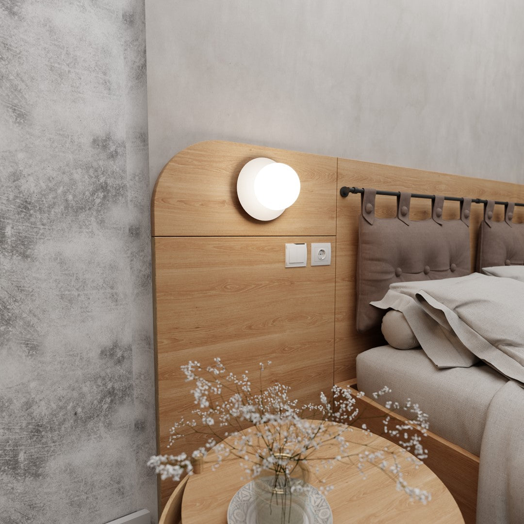 Scène de chambre en vue large avec lit, table et applique murale allumée.