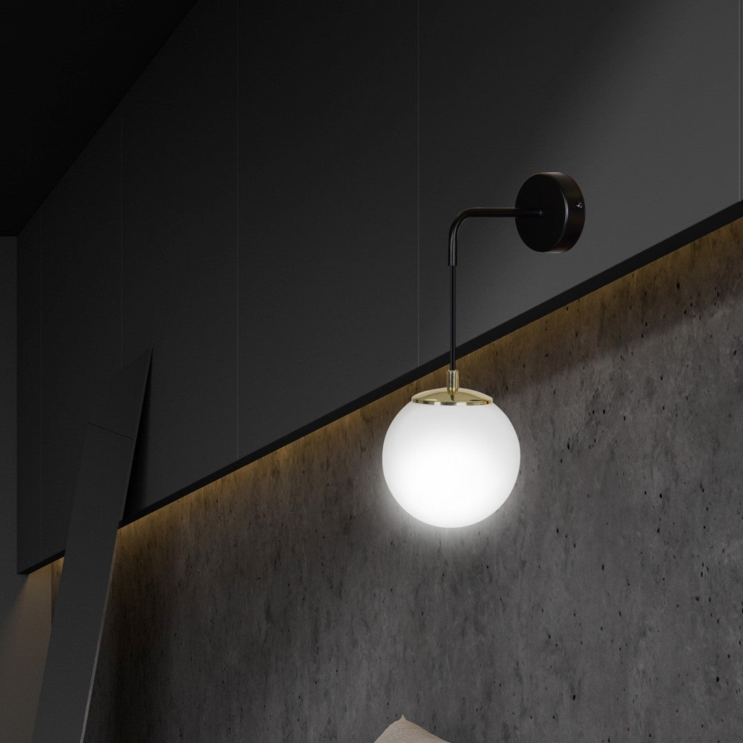 Gros plan du globe lumineux éclairant un mur béton, bras noir et cerclage laiton.