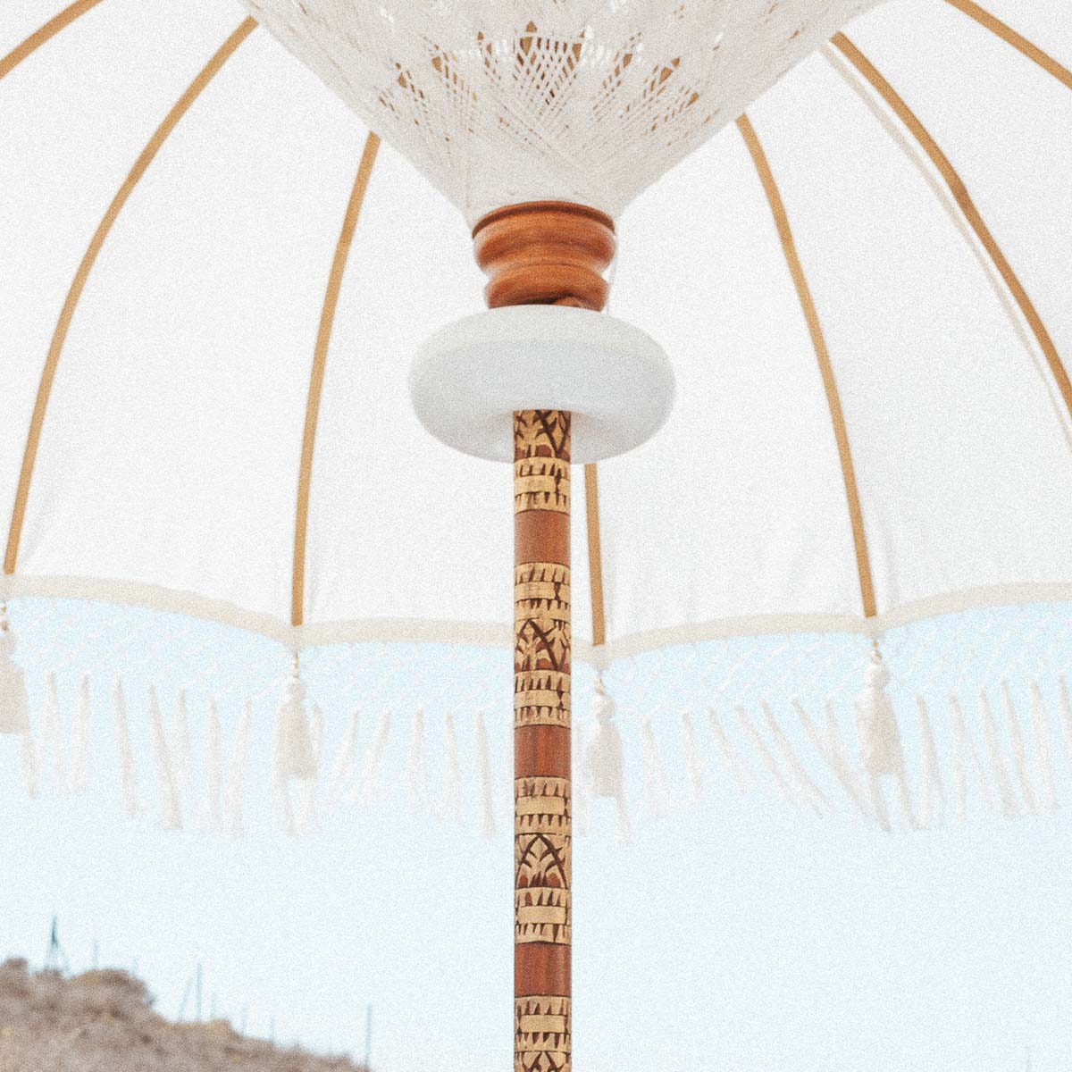 Luminaire éteint sur le mât ouvragé, parasol blanc à pompons sous ciel clair