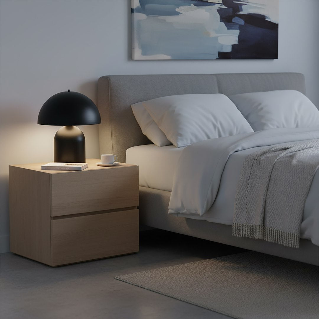 Mise en ambiance dans une chambre, lampe allumée sur chevet en bois près du lit