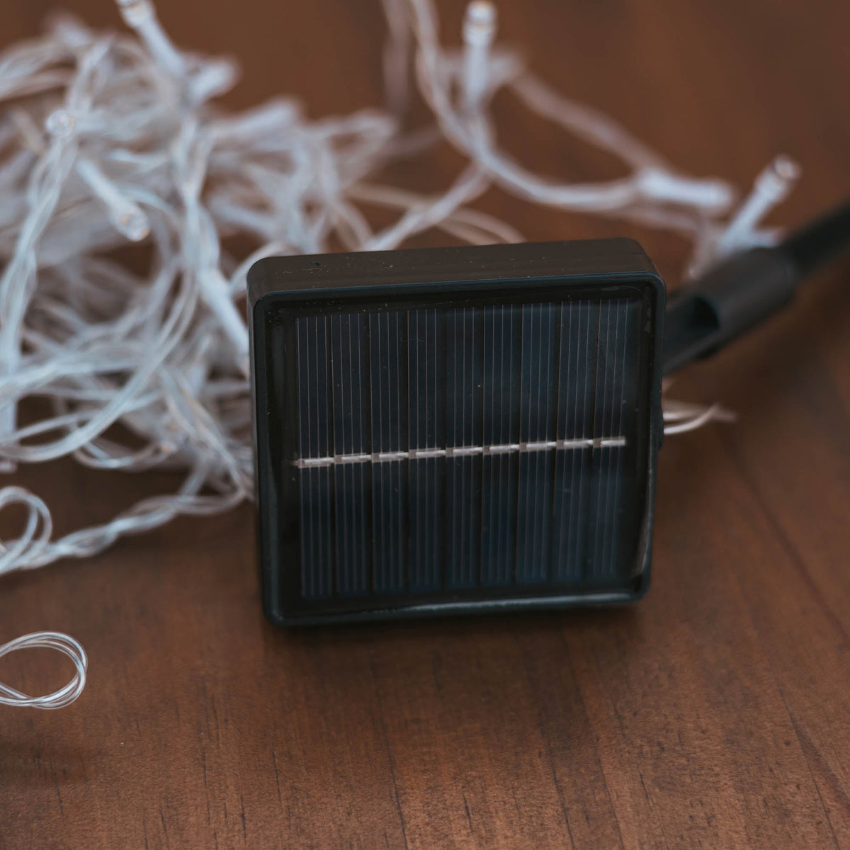 Panneau solaire noir carré posé sur une table en bois avec guirlande emmêlée.