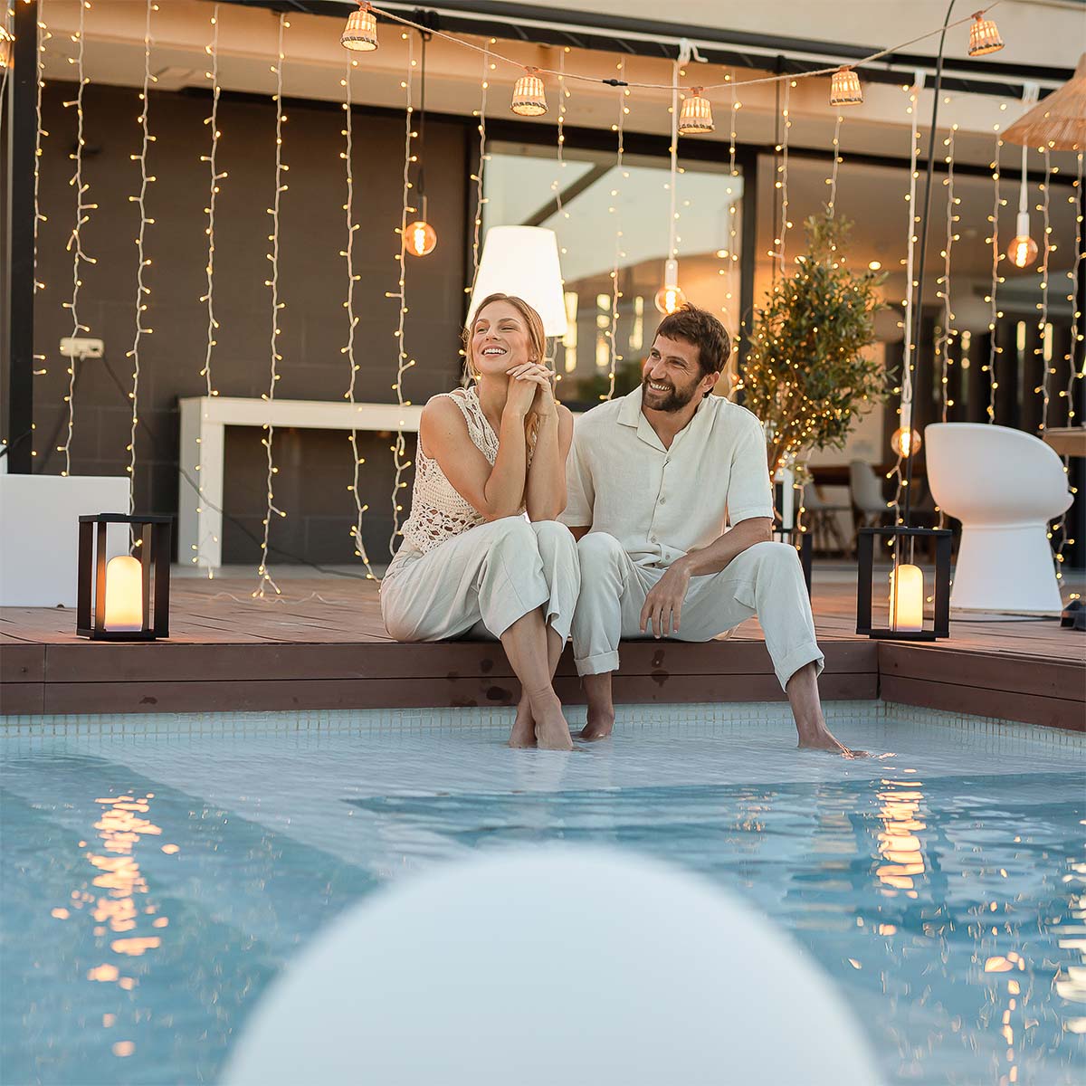 Couple assis au bord d'une piscine sous un rideau de lumières chaudes