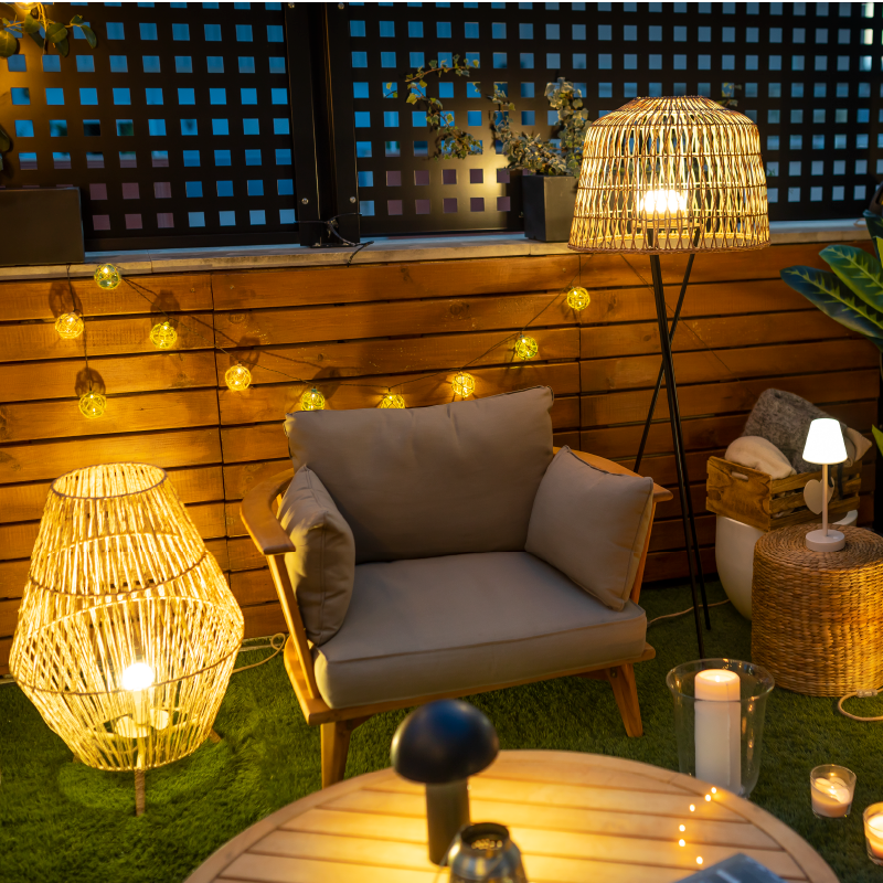 Terrasse aménagée le soir, guirlande tendue, fauteuil et lampes en rotin