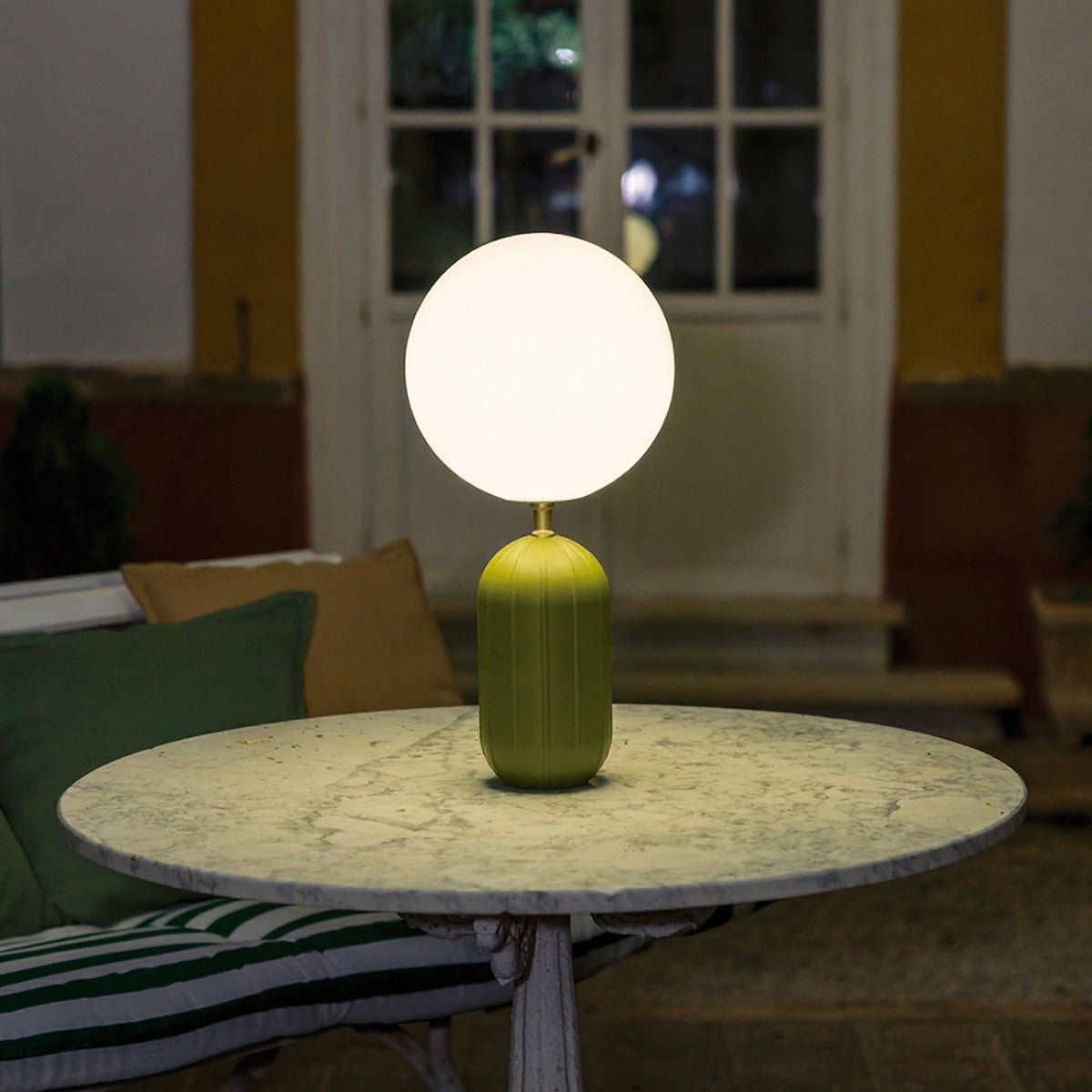 Lampe verte posée sur table ronde en marbre, porte vitrée en arrière-plan