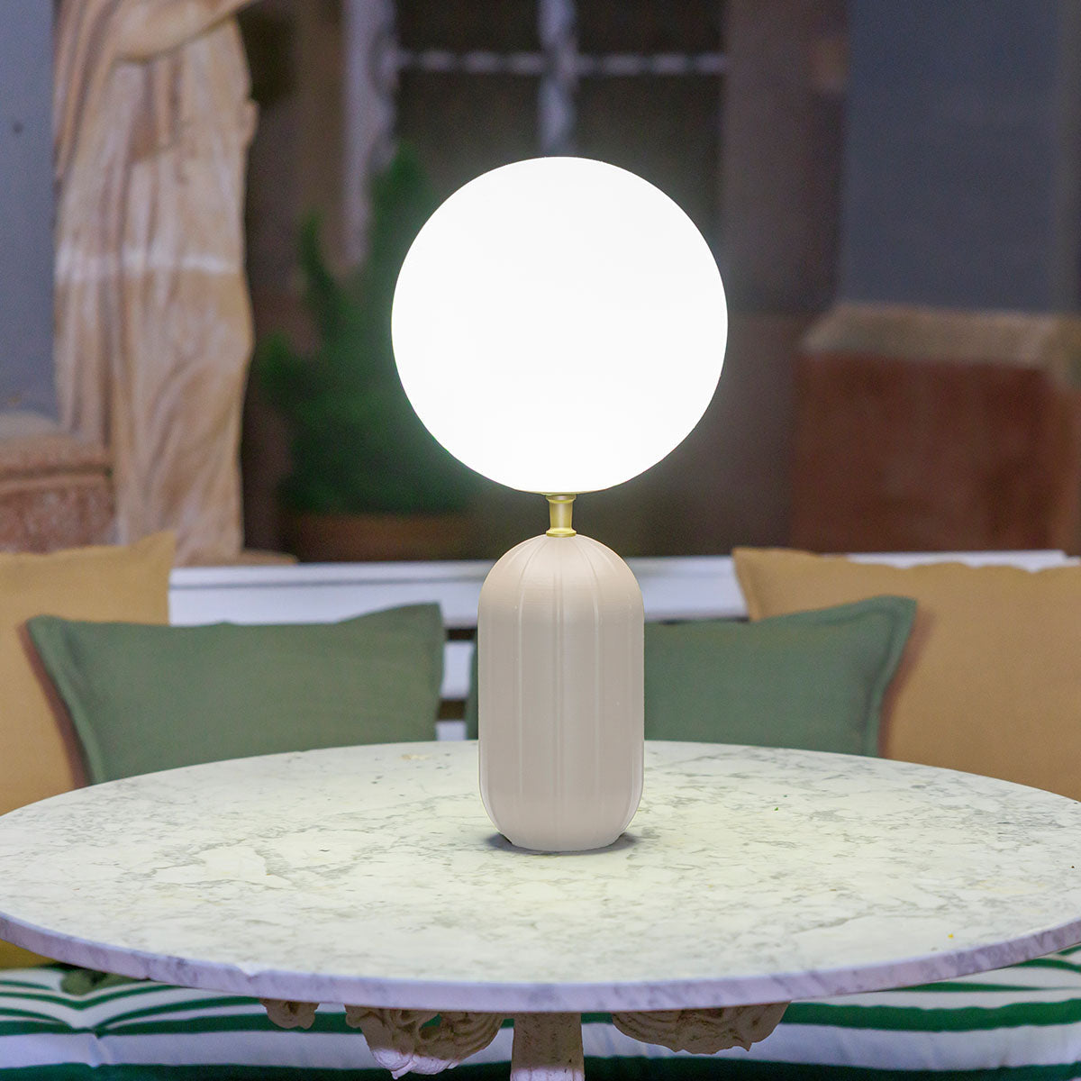 Lampe blanche sur table ronde en marbre, coussins verts et jaunes flous