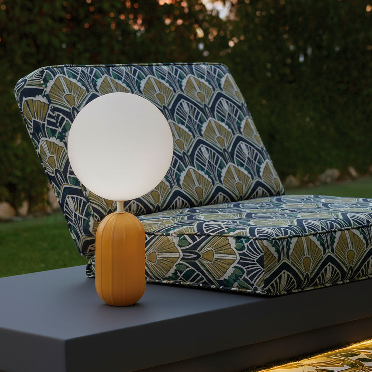 Lampe ocre devant un fauteuil imprimé de motifs Art déco, dans un jardin