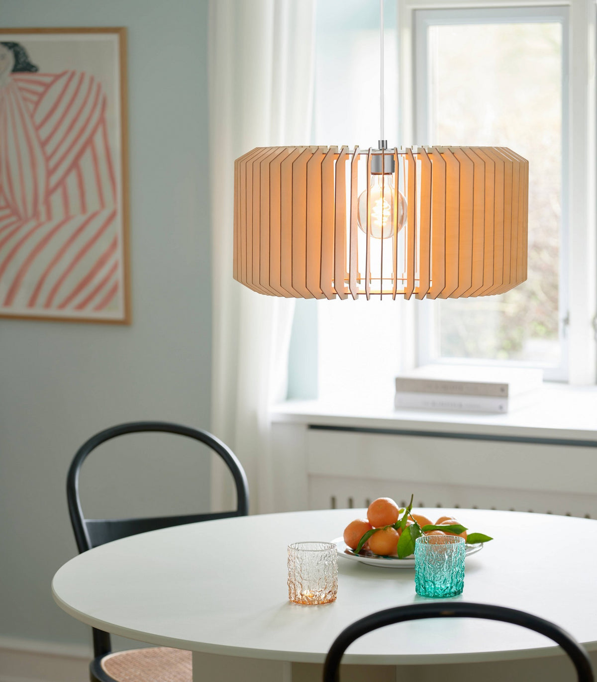 Mise en ambiance au-dessus d'une table ronde avec chaises noires et panier de fruits.
