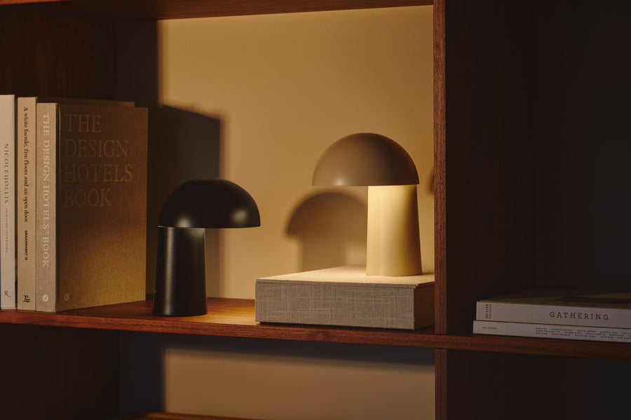 Deux lampes champignon, une noire et une beige, posées sur une étagère avec livres