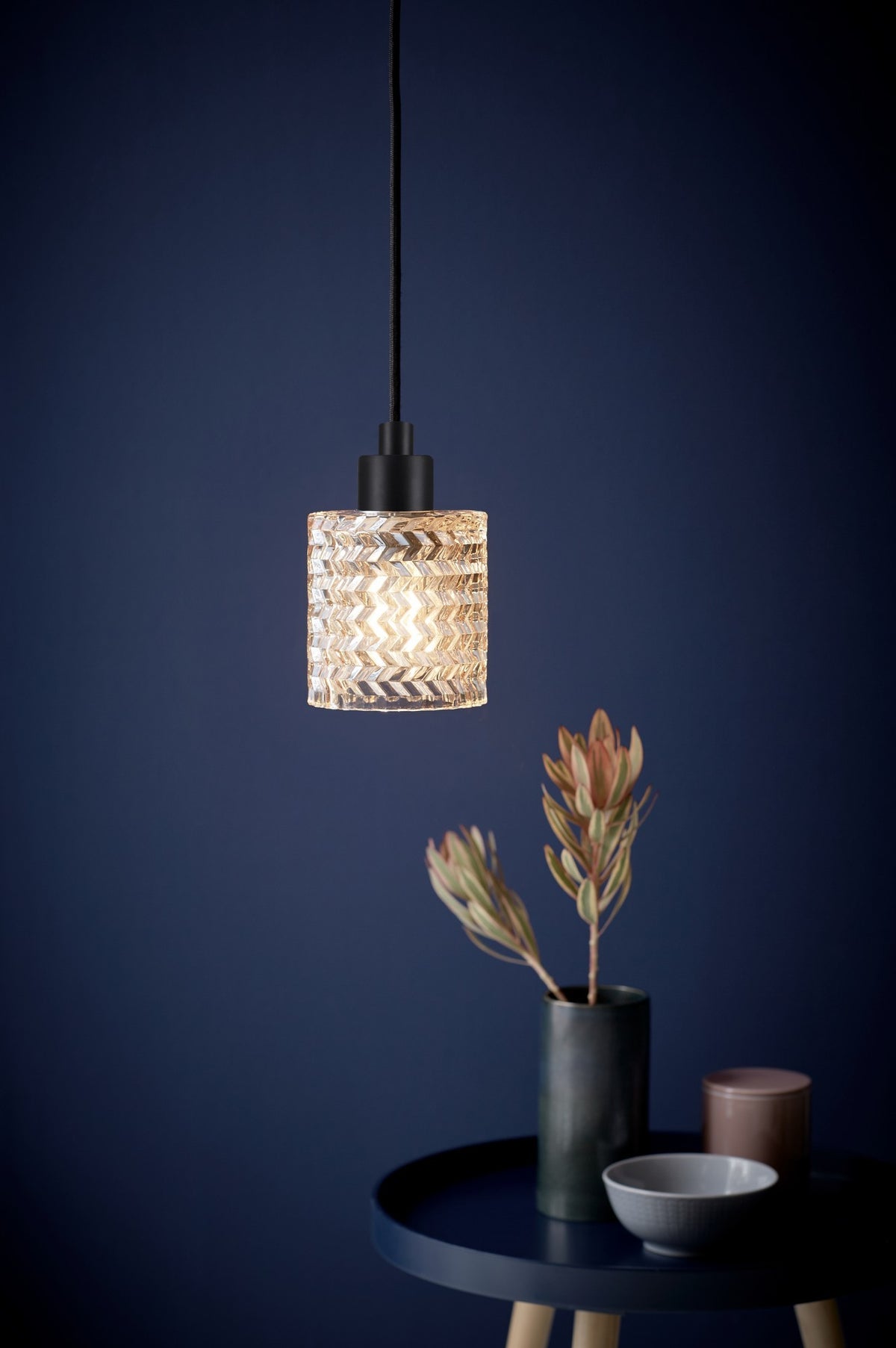 Mise en ambiance du luminaire allumé au-dessus d'une table dans un intérieur bleu nuit