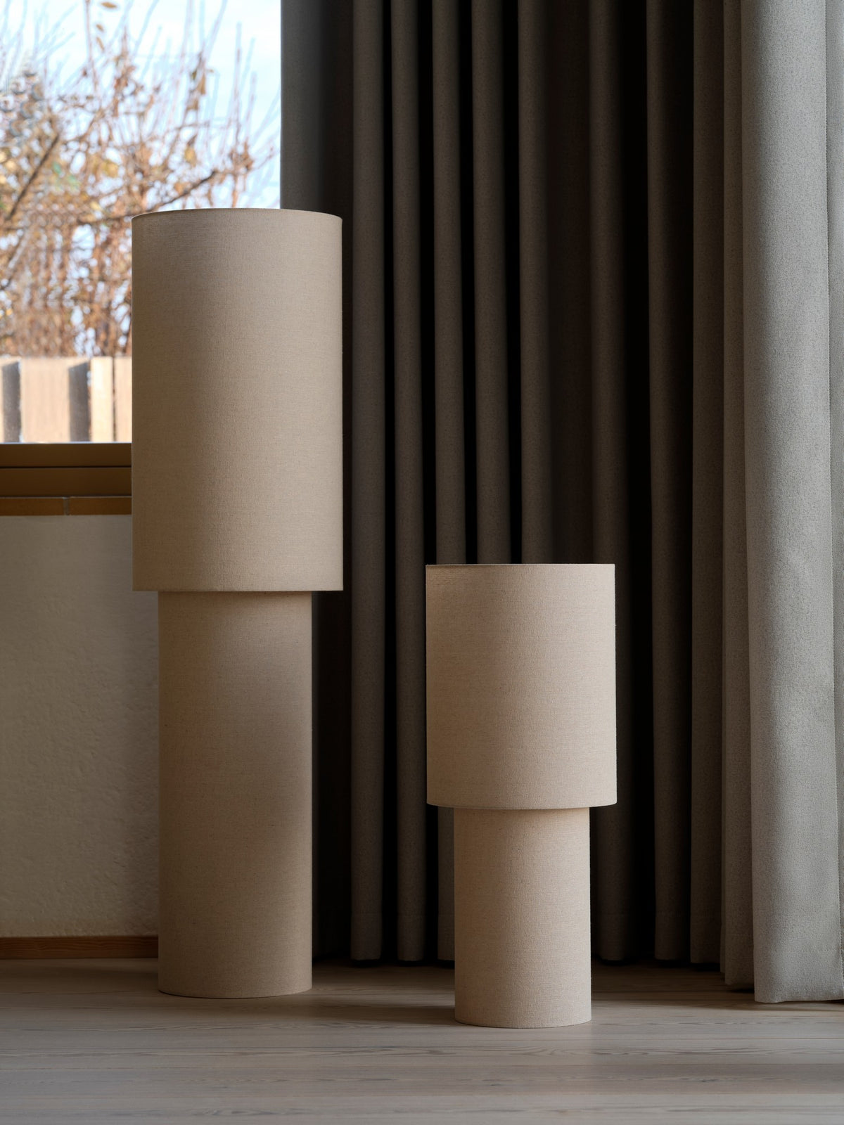 Deux lampadaires cylindriques de hauteurs différentes côte à côte près des rideaux.
