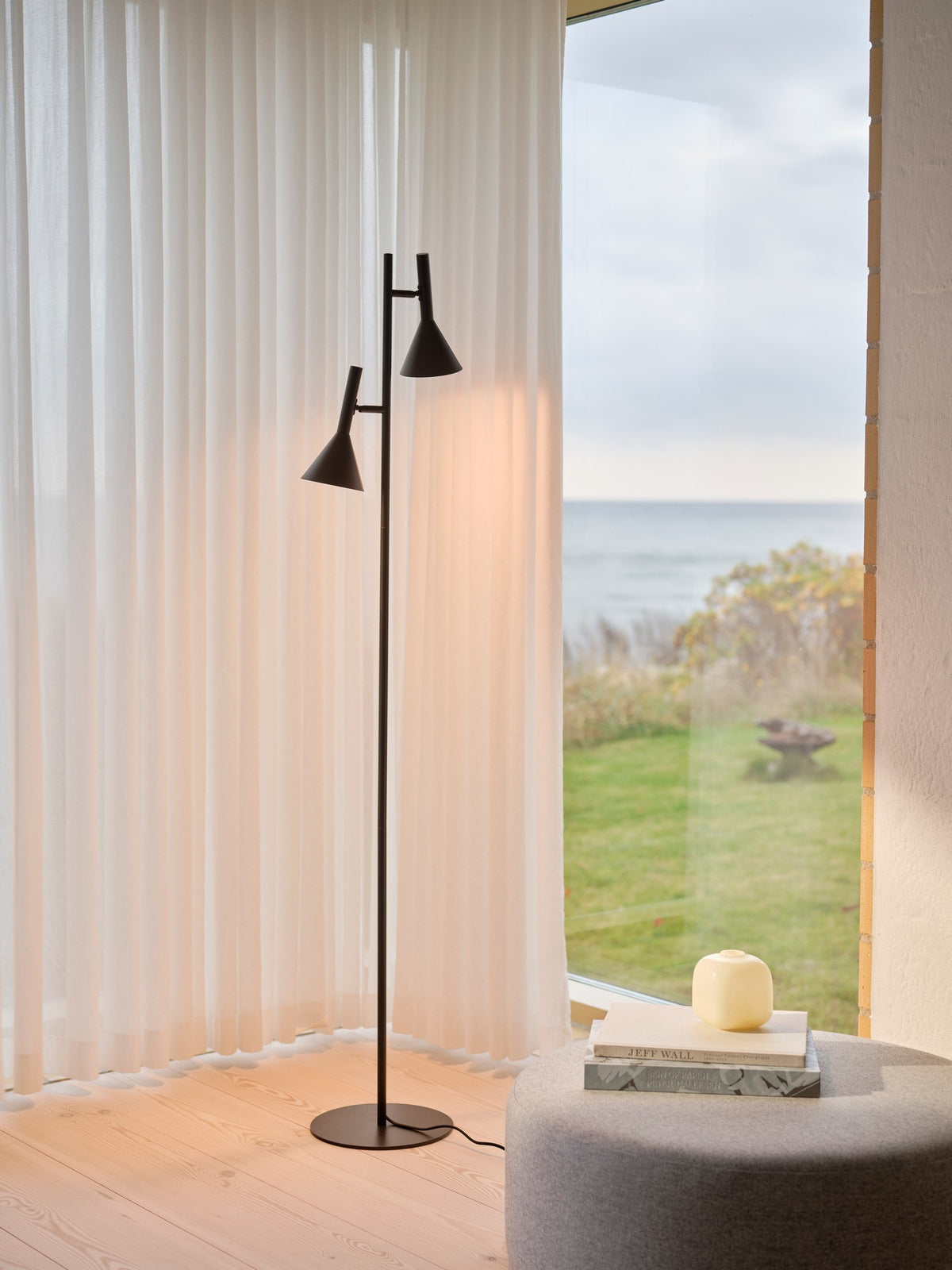 Lampadaire allumé dans un salon près d'une fenêtre et d'un pouf