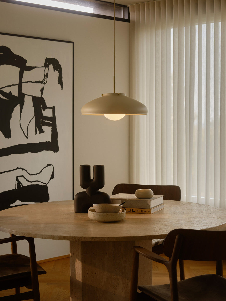 Suspension allumée au-dessus d’une table à manger, intérieur contemporain avec rideaux et tableau.