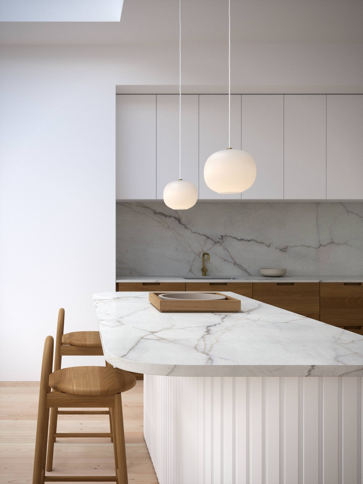 Mise en ambiance dans une cuisine moderne avec îlot en marbre et deux suspensions blanches.