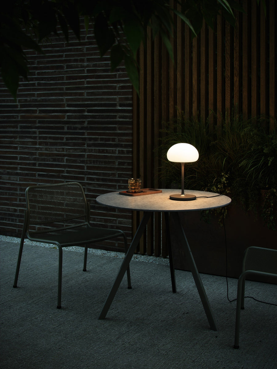 Lampe sur table extérieure en terrasse, devant mur de briques et plantes.