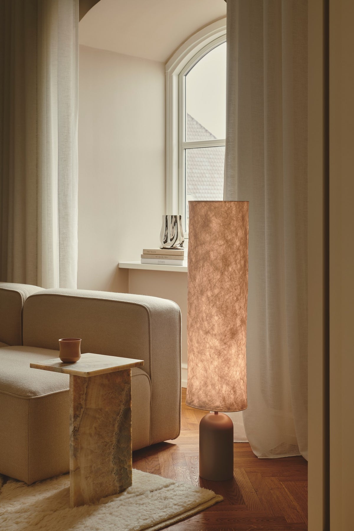 Mise en ambiance : lampadaire allumé près d'un canapé beige et d'une fenêtre.