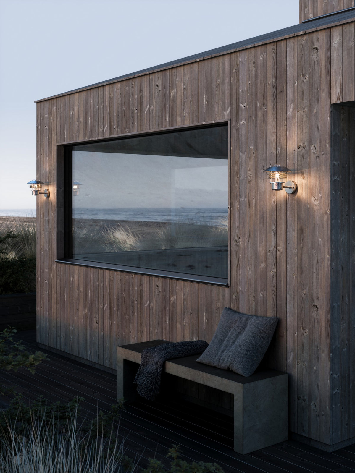 Mise en ambiance sur façade de bois sombre face à la mer, deux appliques allumées