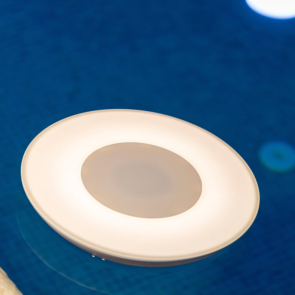 Gros plan sur l'anneau lumineux et la grille centrale d'une enceinte ronde immergée.
