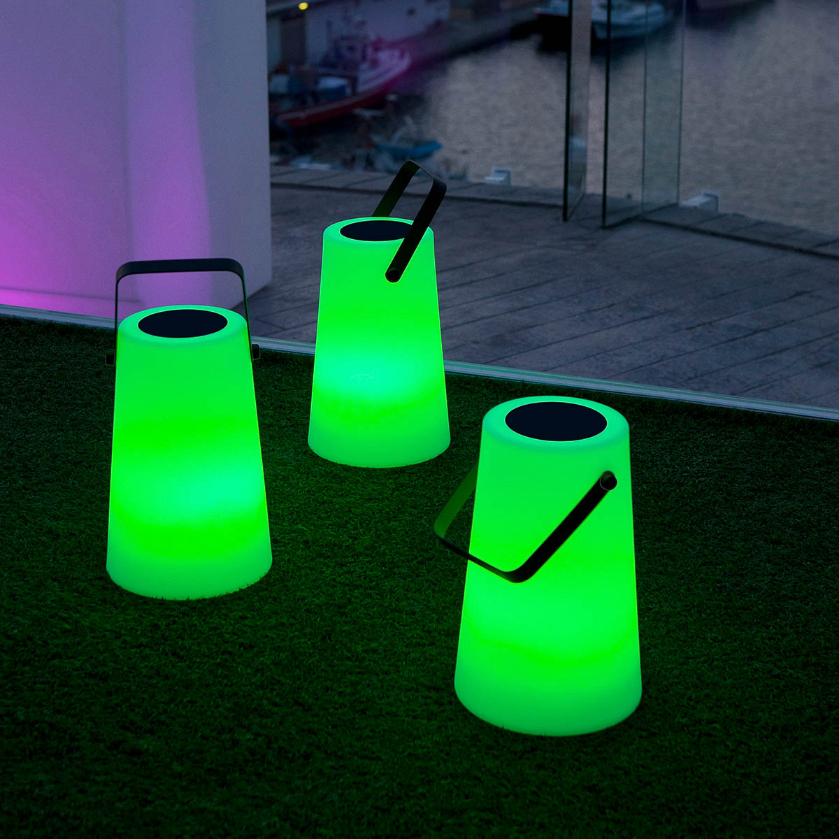 Trois lampes portatives vertes posées sur gazon artificiel près d'une baie vitrée