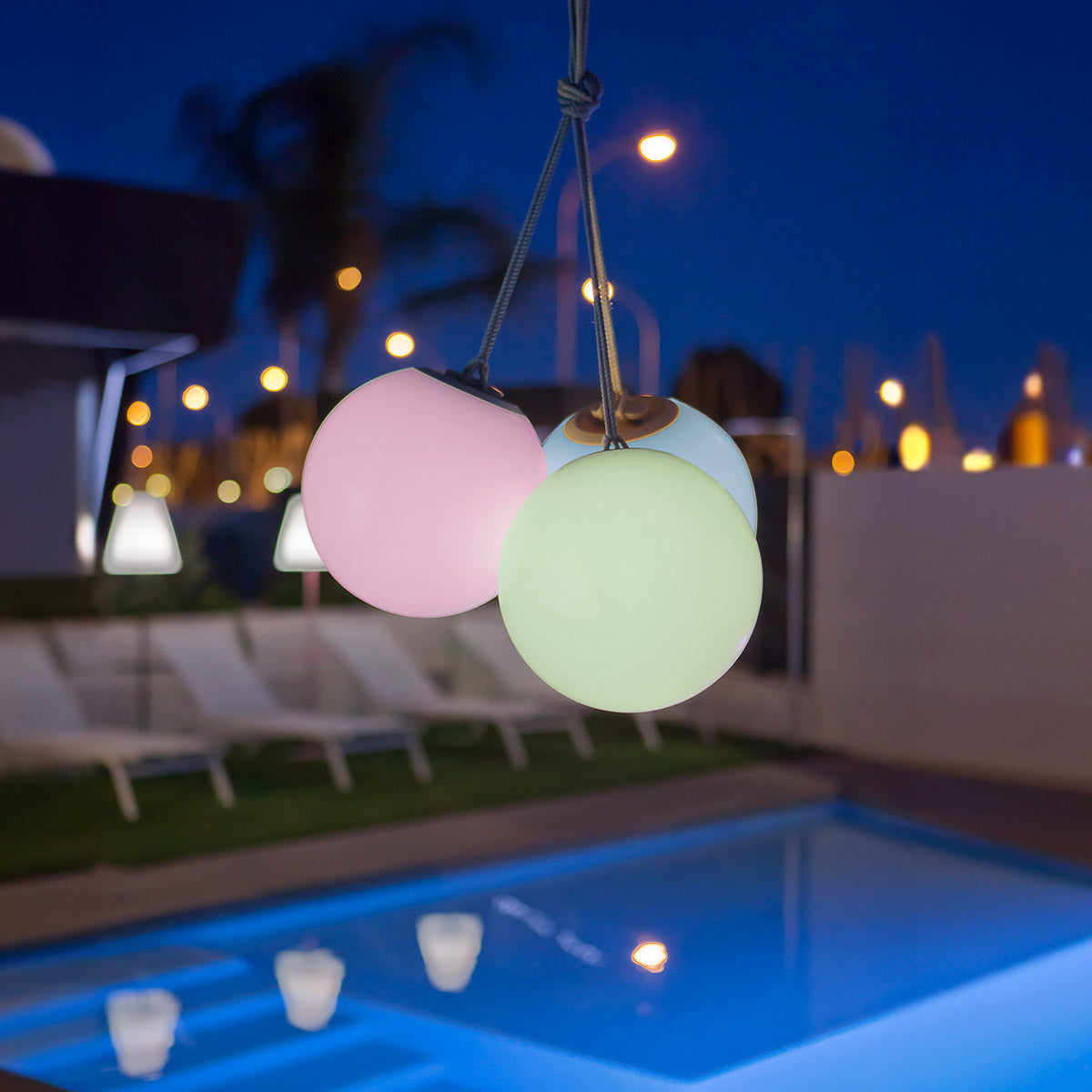 Trois globes lumineux colorés suspendus au-dessus d'une piscine la nuit