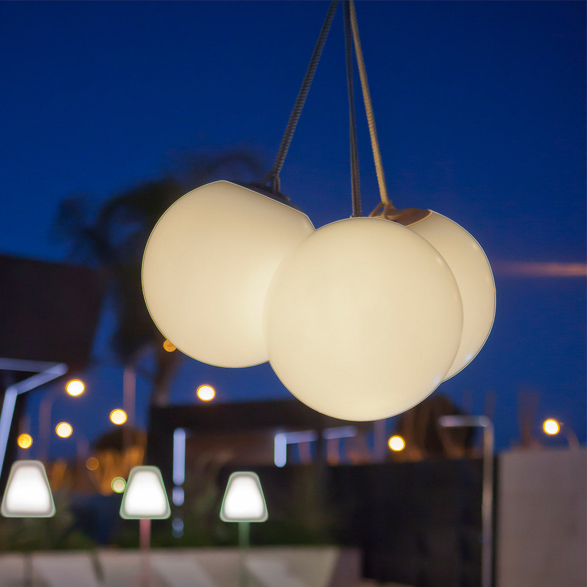 Gros plan sur trois globes lumineux suspendus par cordon, fond bleu nuit