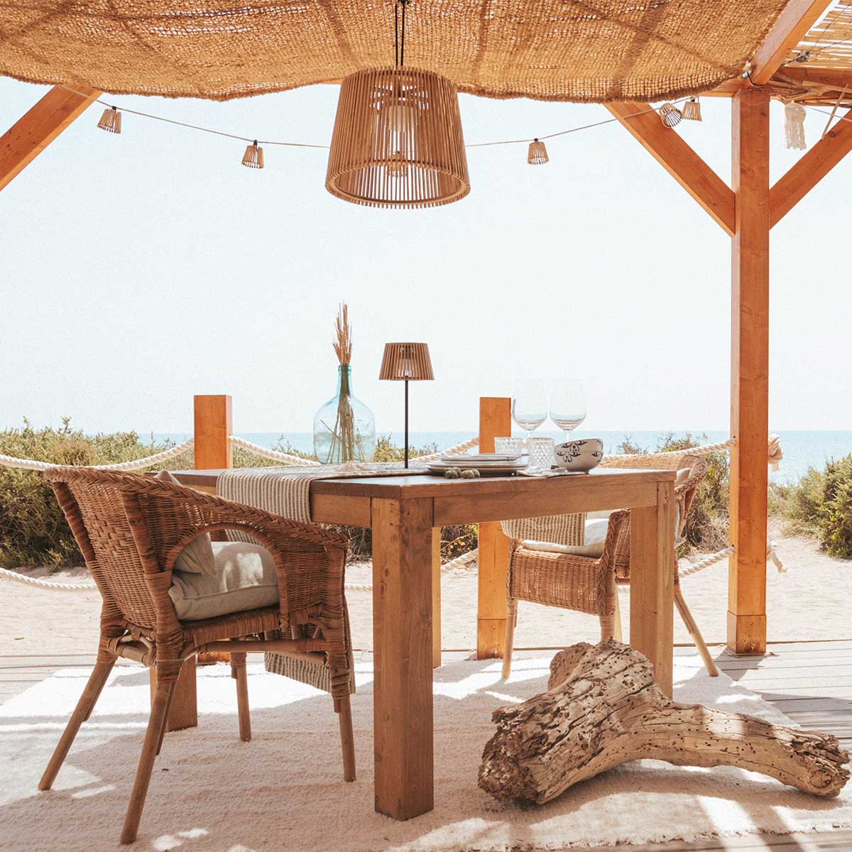 Mise en ambiance sur terrasse en bois face à la mer, table et suspensions