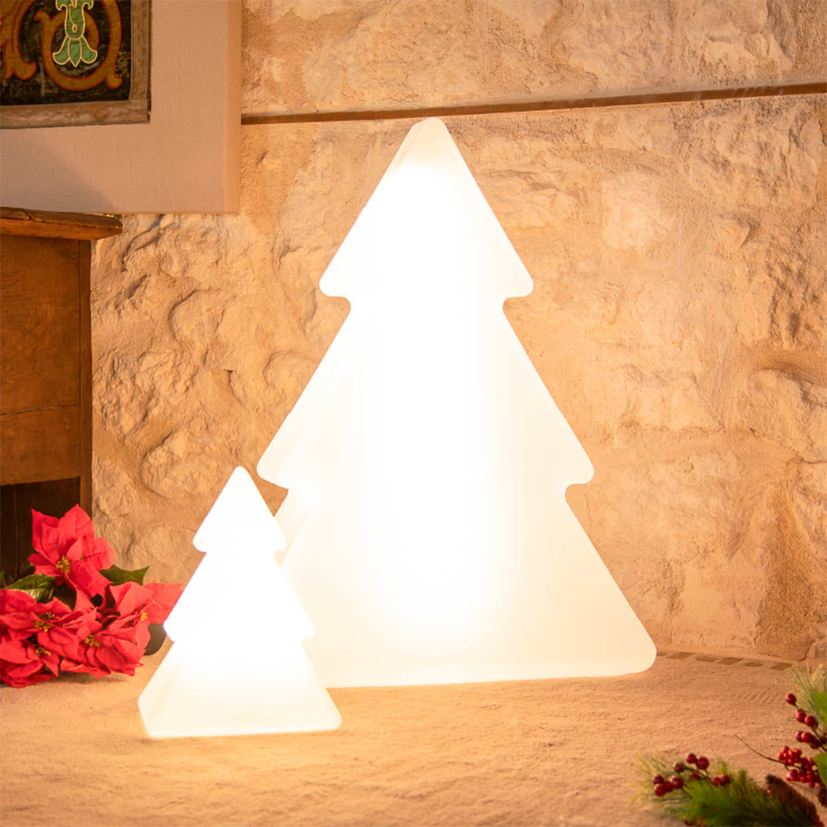 Deux sapins lumineux allumés devant un mur de pierre, près d'une cheminée et de poinsettias