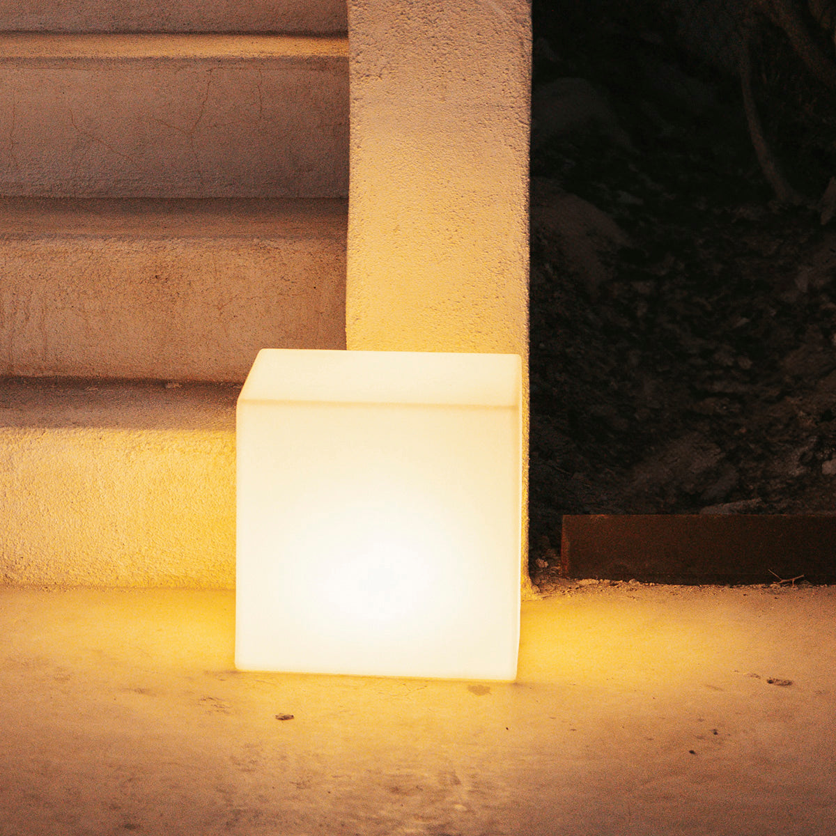 Cube lumineux ambré posé devant des marches de béton, ambiance nocturne extérieure