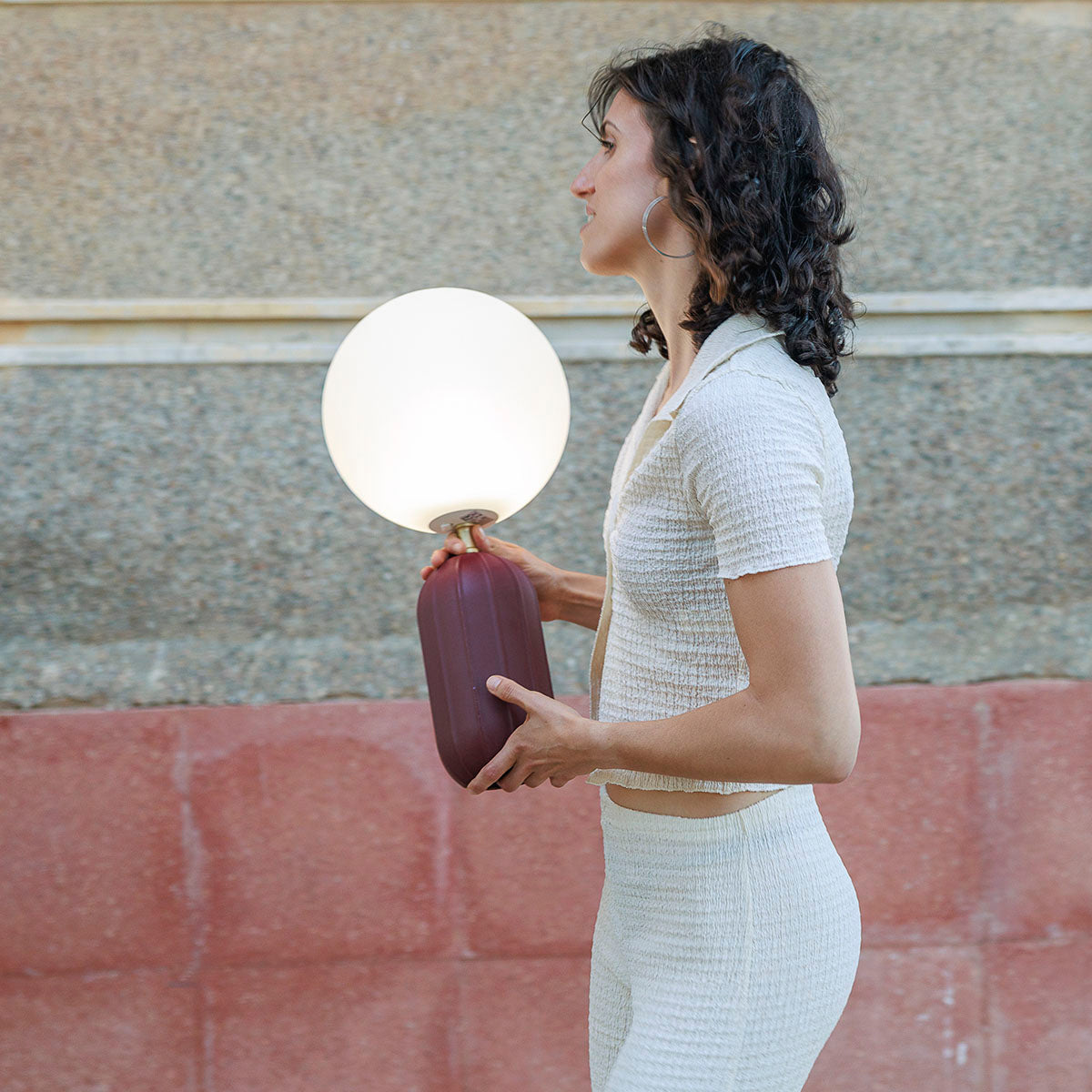 Femme tenant la lampe bordeaux à la main, vue de profil, base cannelée