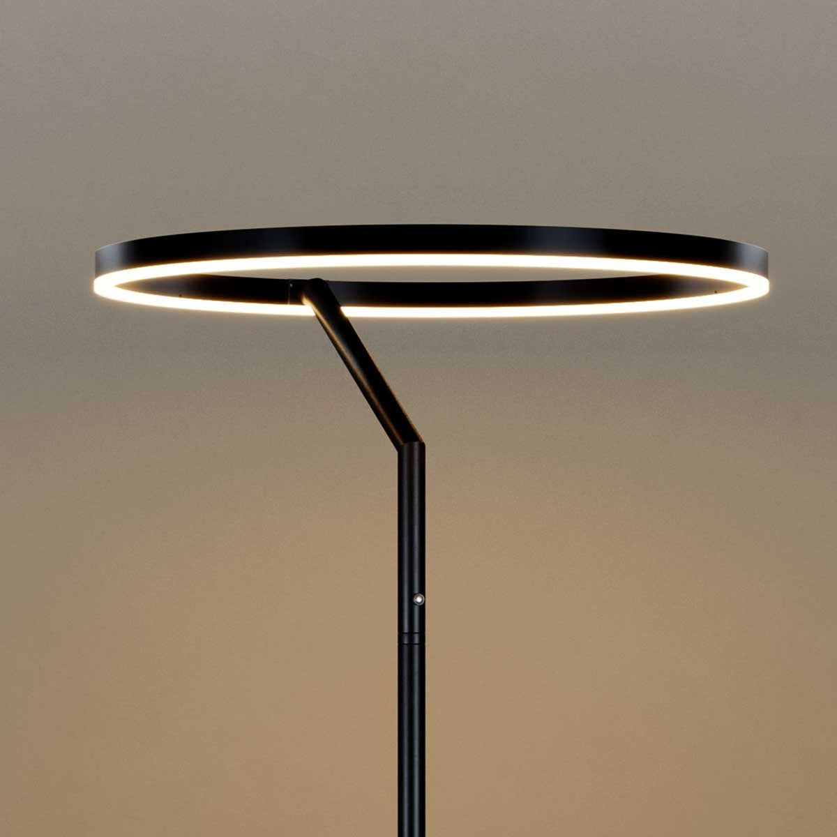 Vue de face du luminaire éteint, anneau noir et tige inclinée sur fond beige.