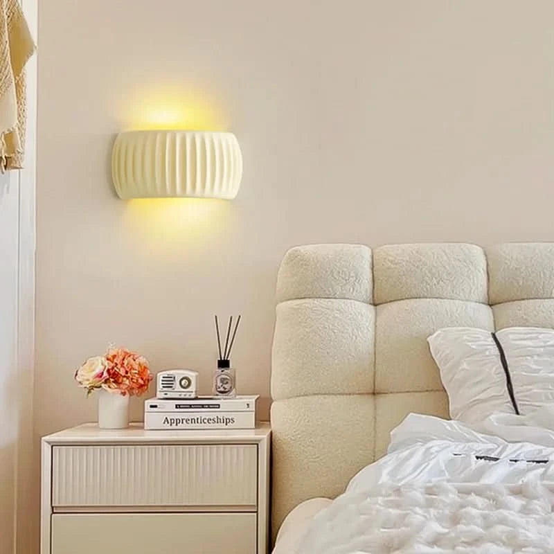 Applique murale crème rainurée au-dessus d'une table de nuit avec livres et fleurs.