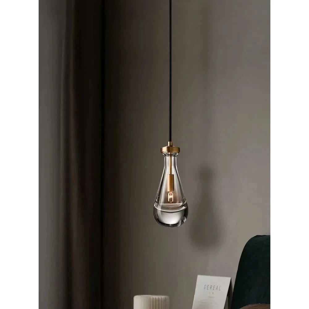 Gros plan sur une suspension en verre transparent, douille dorée et ampoule allumée, ombre portée.