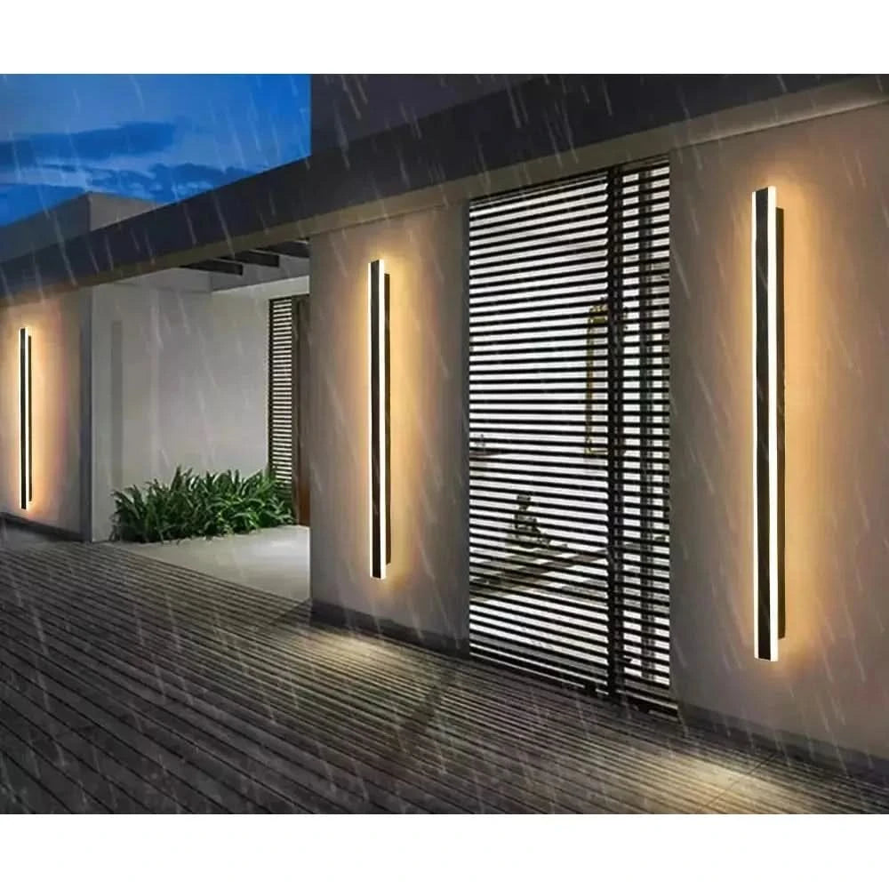 Trois appliques linéaires verticales éclairant un mur de terrasse sous la pluie
