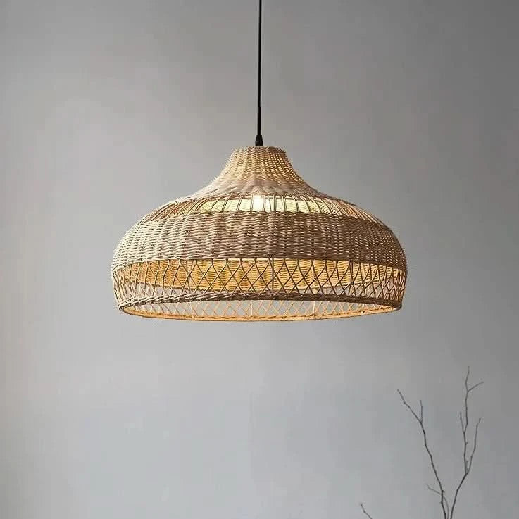 Mise en ambiance sur mur gris, suspension rotin allumée près d'une branche décorative.