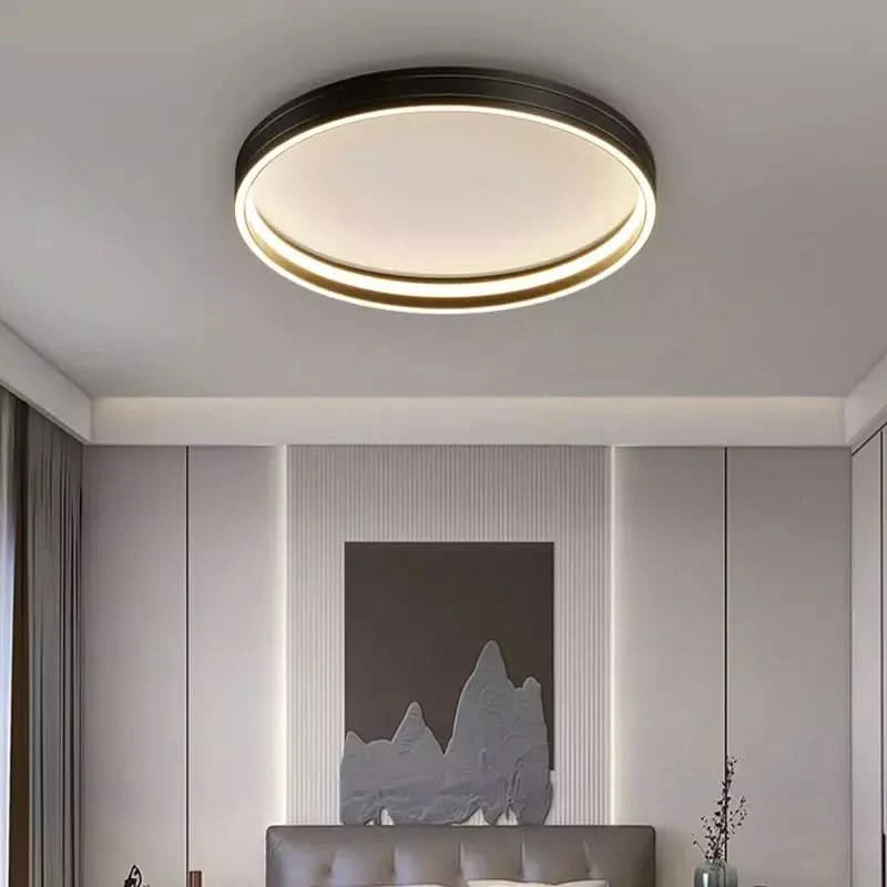 Plafonnier rond à bord noir, éclairé, au-dessus d'un lit avec tête de lit.