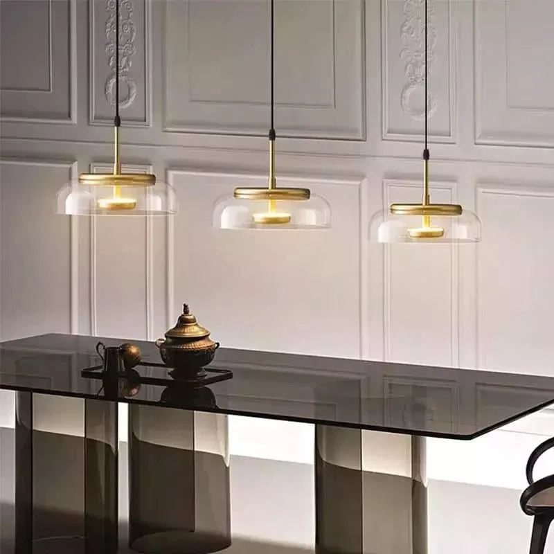 Trois luminaires alignés devant un mur mouluré blanc, au-dessus d'une table noire