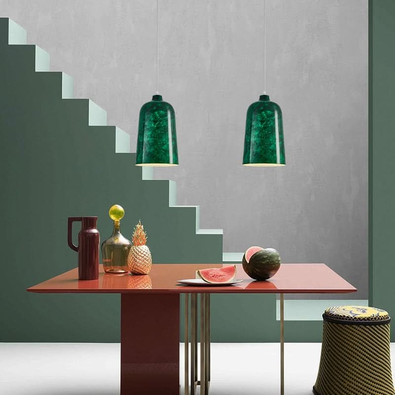 Deux suspensions vertes éclairant une table rouge dans un décor aux marches graphiques.